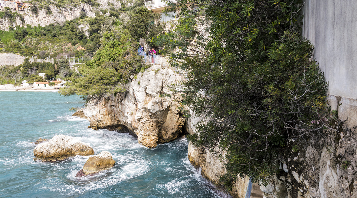 People standing on a ledge cut into a cliffside watching the sea swirl around the rocks below